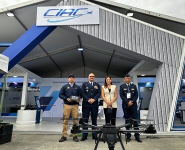 Cuatro personas (ANDRÉS GÓMEZ INGENIERO CIAC, MG ANDRÉS GUZMÁN PRESIDENTE CIAC, ANA CATALINA CANO, VICEMINISTRA GSED, Y CORONEL TAVERA GERENTE DE DISEÑO Y DESARROLLO CIAC) frente al stand de CIAC en la feria F-AIR 2025, delante de ellos el DRAGOM en el suelo