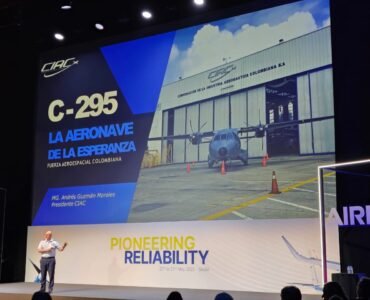 EL MG ANDRÉS GUZMÁN dando un discurso en la CONFERENCIA DE OPERADORES DE EQUIPO C-295 y CN-235 con la presentación al fondo en una pared grande donde se ve una aeronave C-295 frente al hangar de CIAC